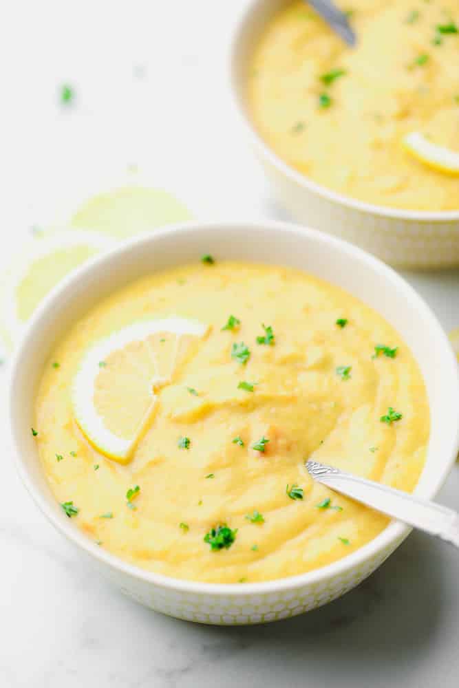 two bowls of yellow soup with a lemon slice on top and parsley