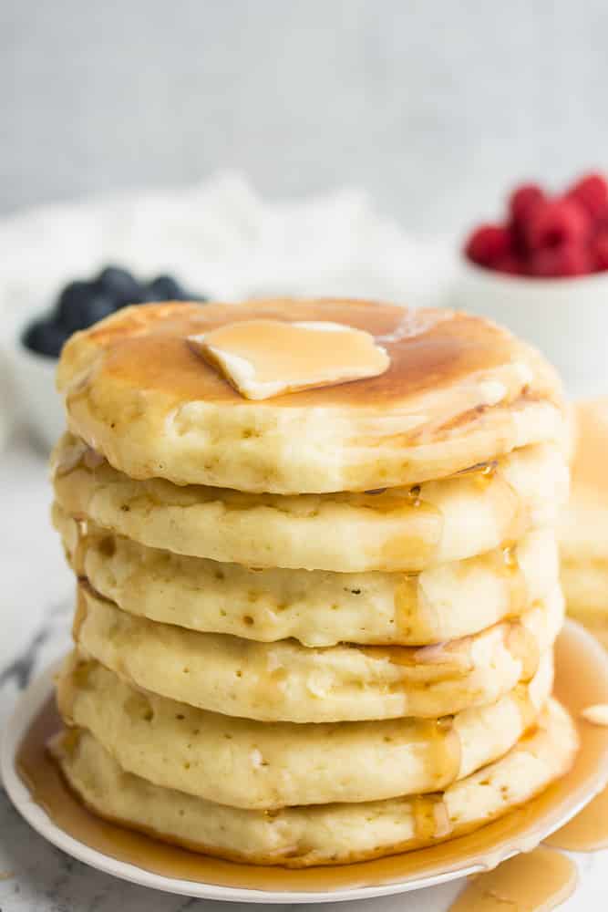 stack of pancakes on a white plate, berries in background