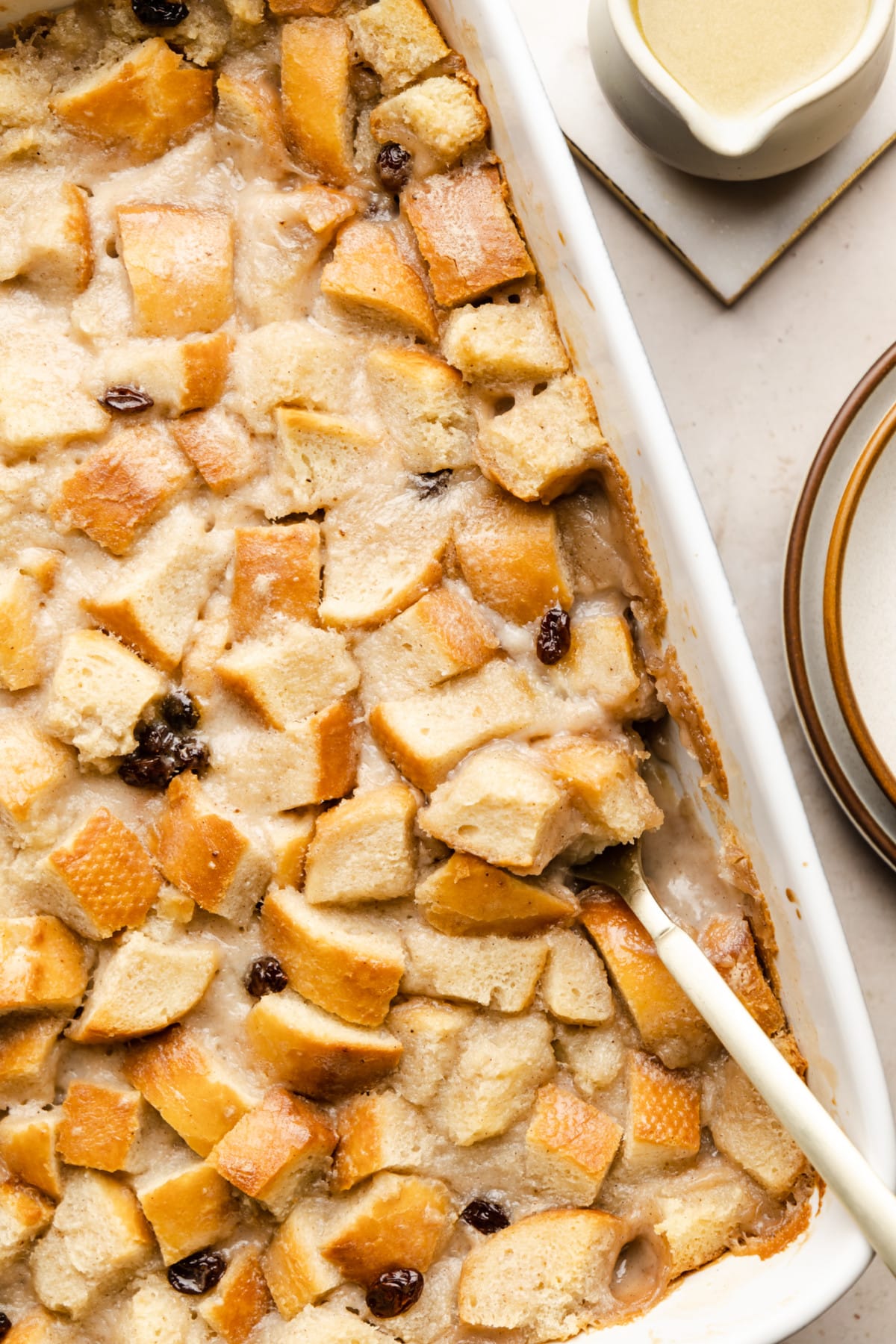 a spoon taking a scoop of vegan bread pudding out of a white baking dish.