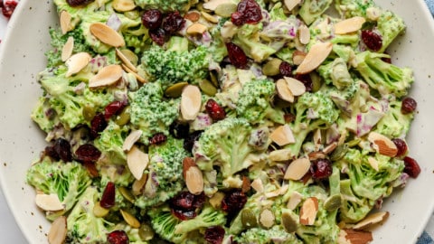 close up on vegan broccoli salad tossed in creamy dressing and topped with almonds in a large white bowl.