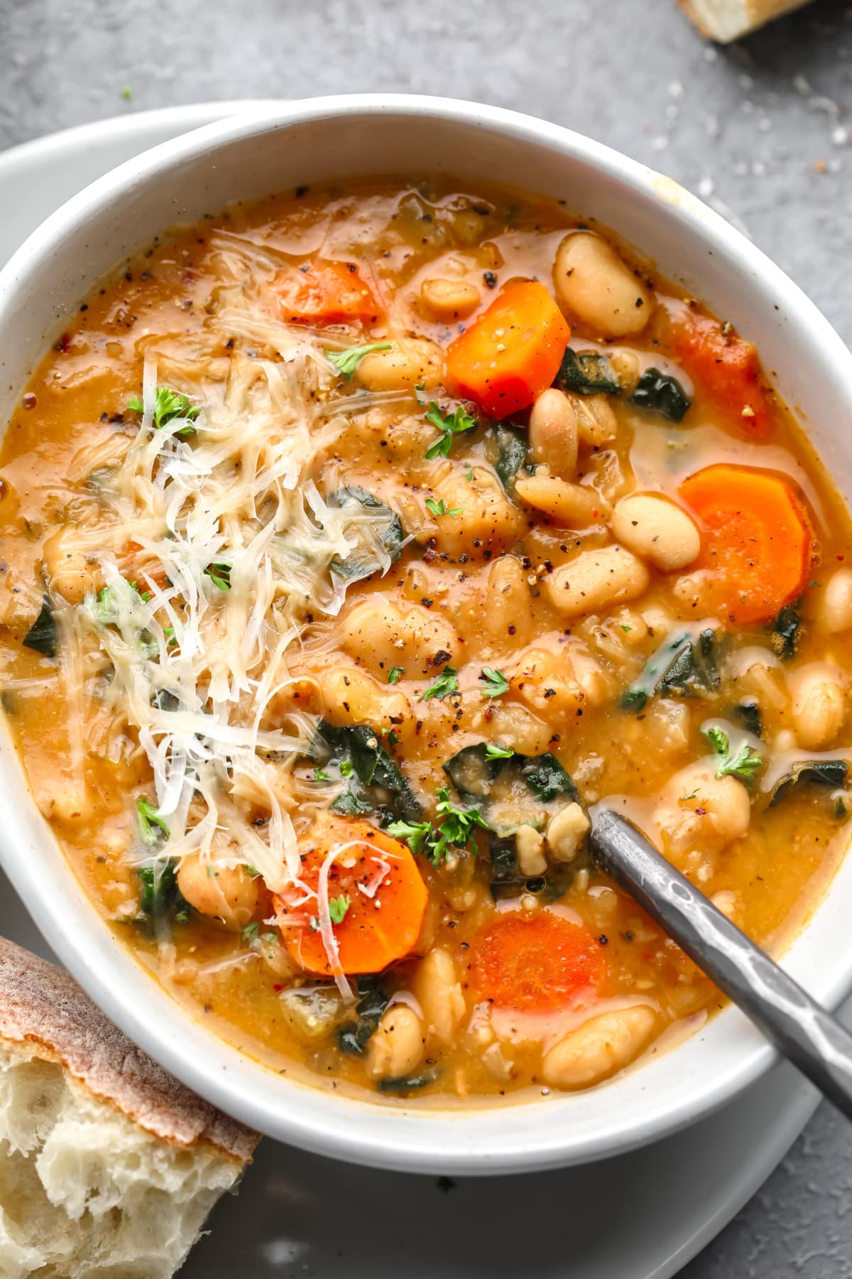 a white bowl full of white bean soup topped with shredded vegan parmesan.