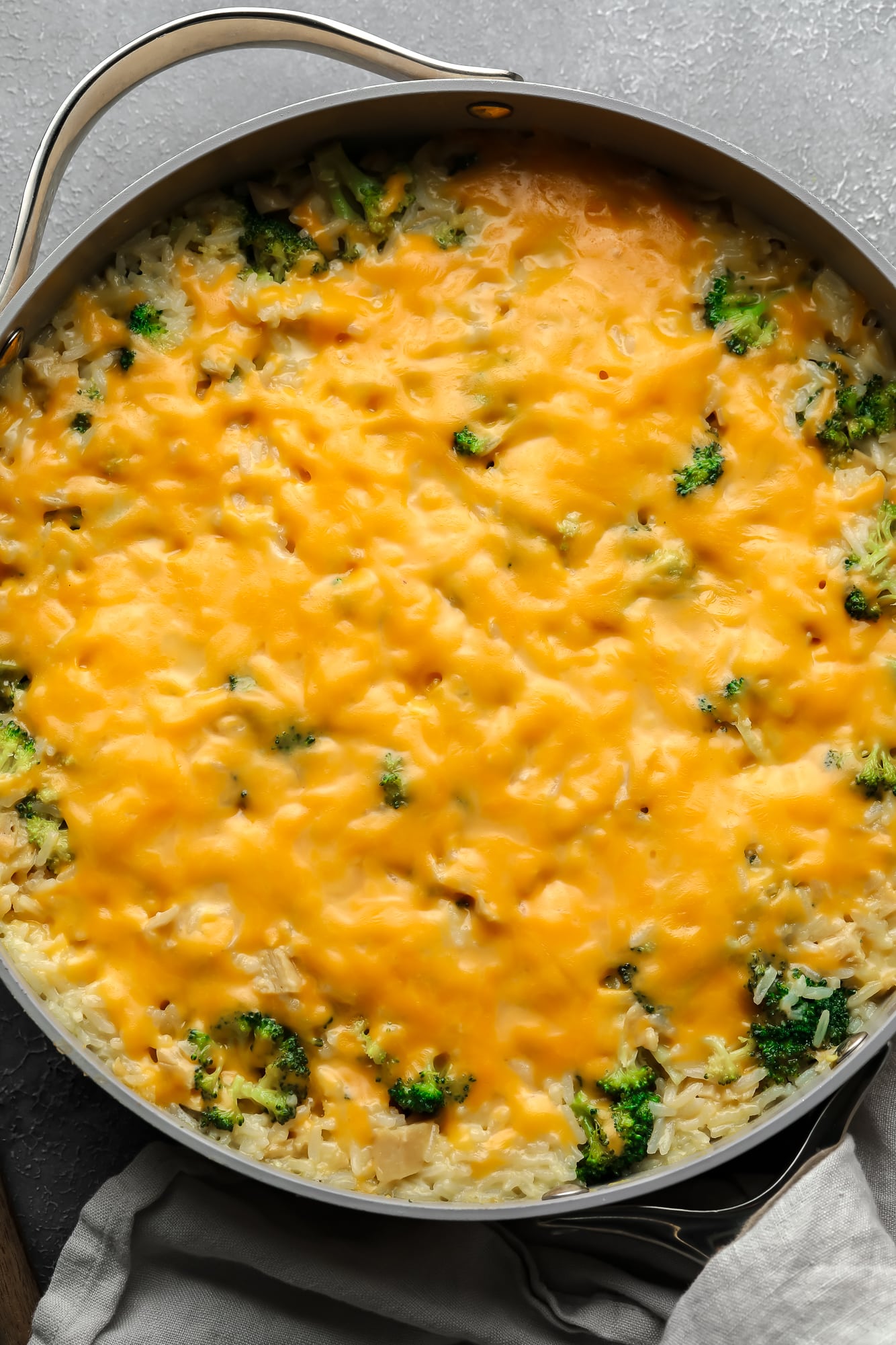 a cheese-covered broccoli and rice vegan casserole in a large skillet.