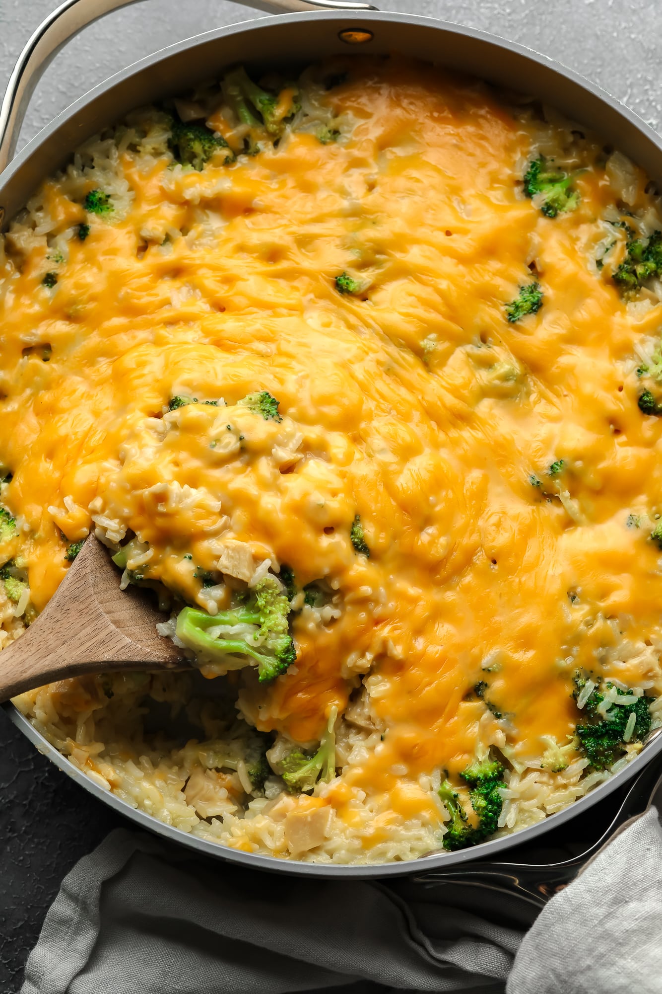a wooden spoon in a cheese-covered broccoli and rice vegan casserole.