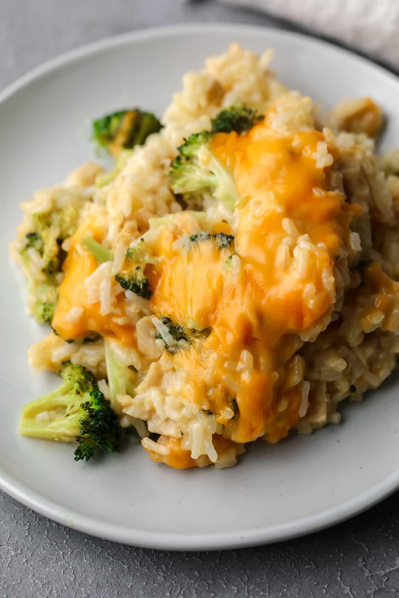 A scoop of a cheese-covered broccoli and rice vegan casserole on a small grey plate.