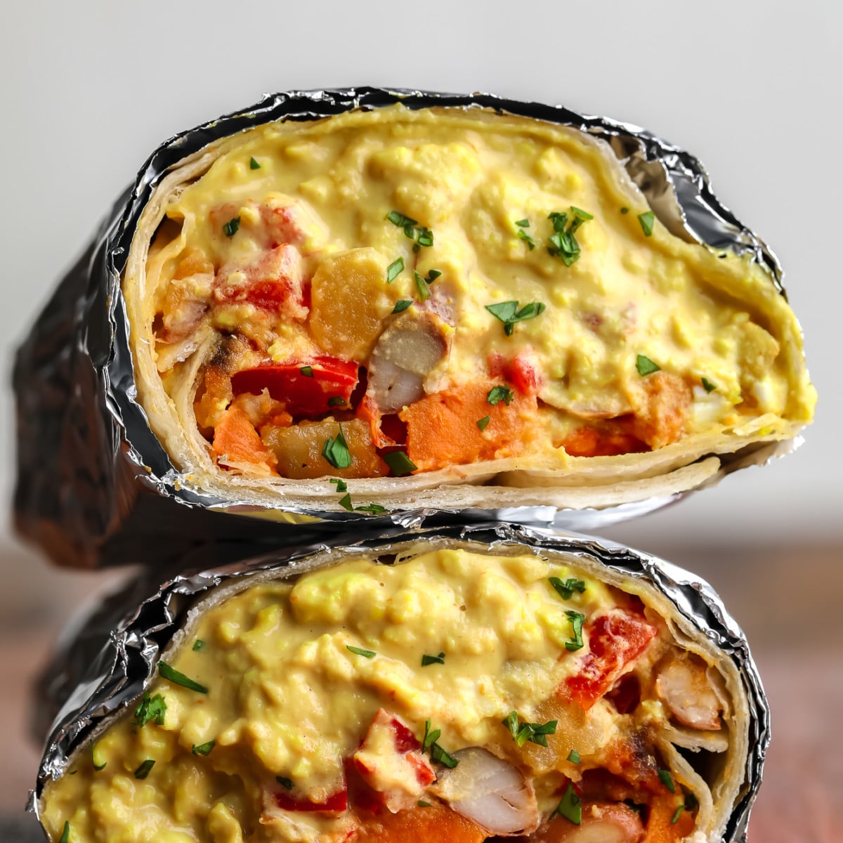 square image of a close up vegan breakfast burrito with eggy mixture and potato veggies