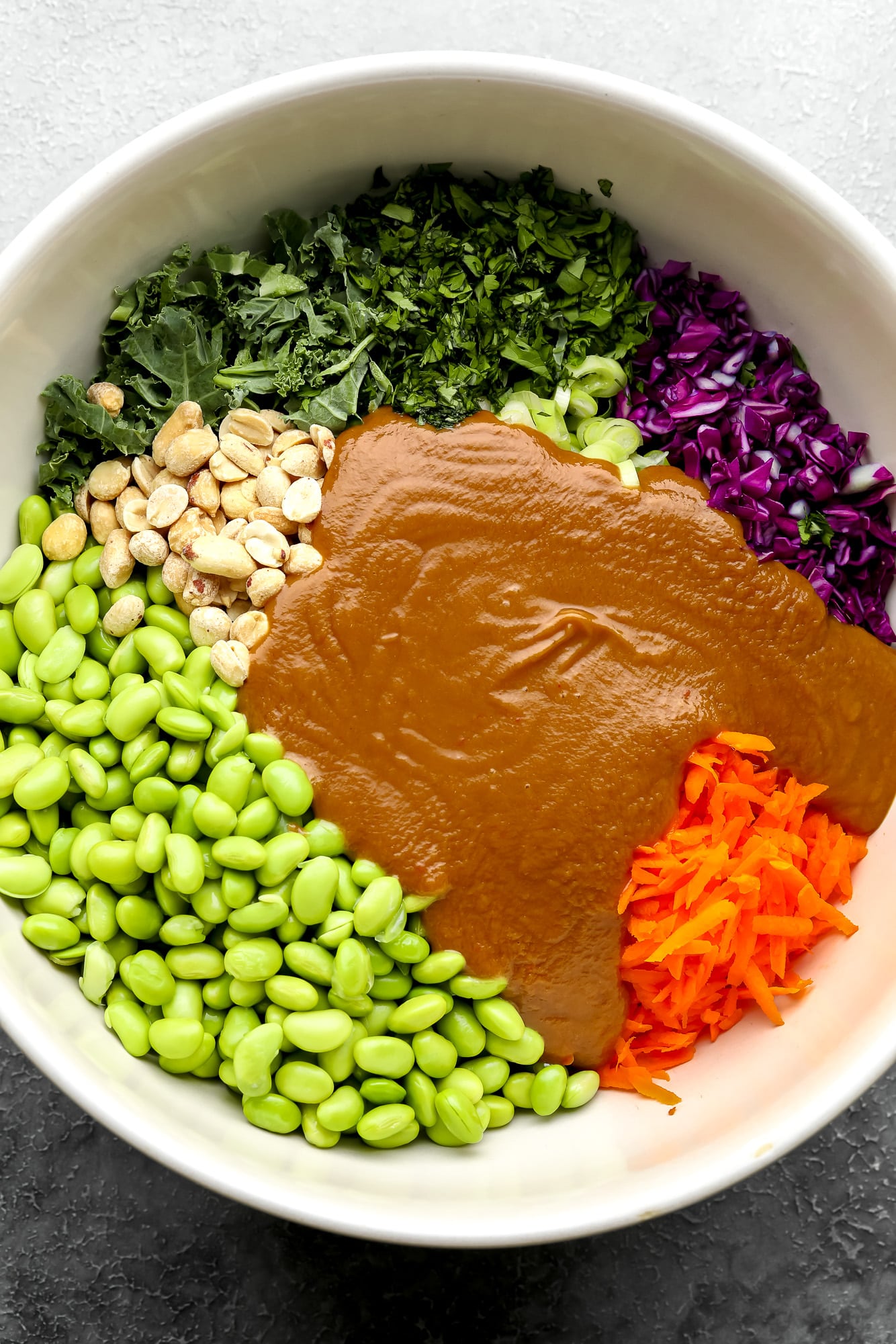 the ingredients for edamame salad covered in peanut sauce in a large white bowl.