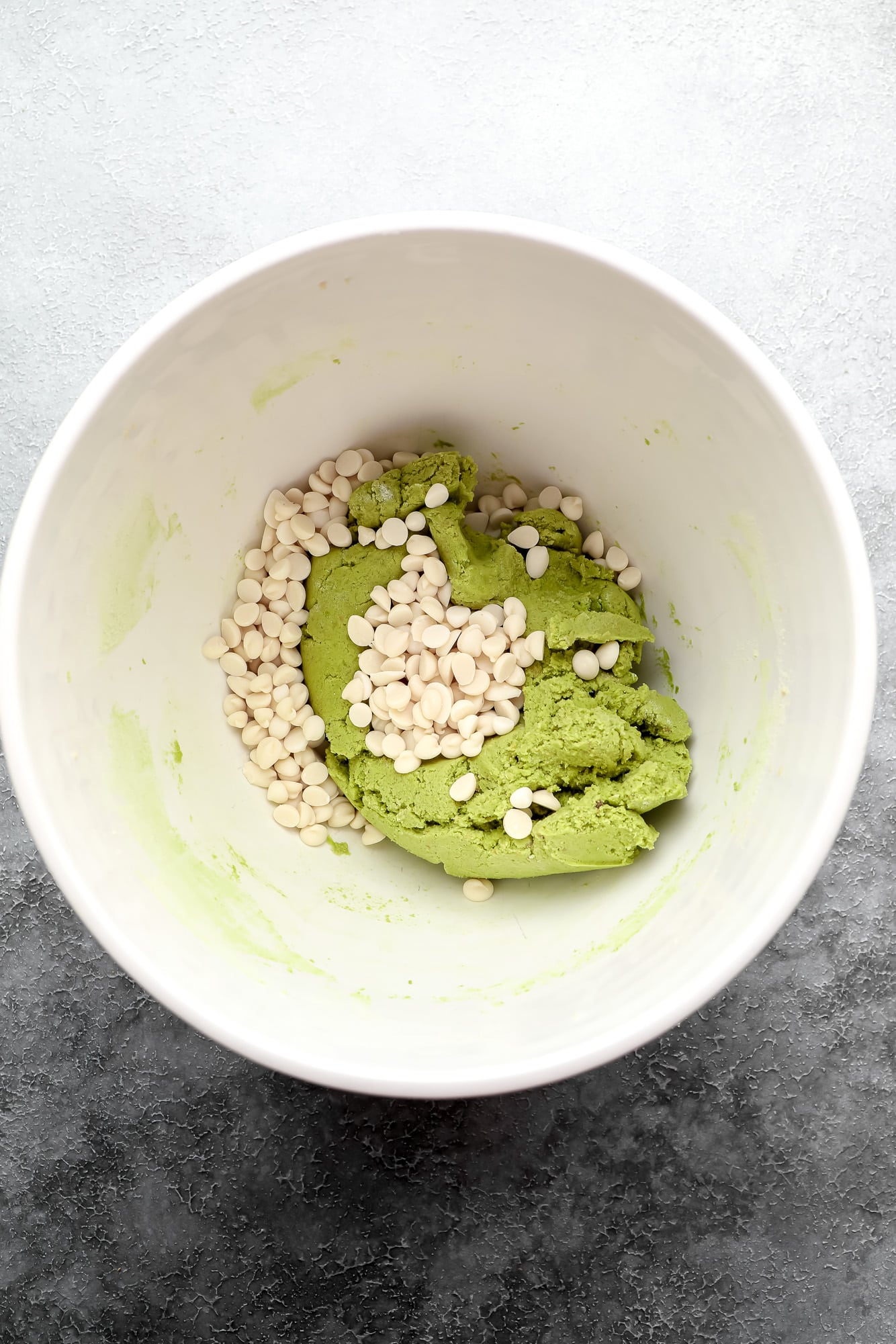 folding white chocolate chips into bright green matcha cookie dough in a white bowl.