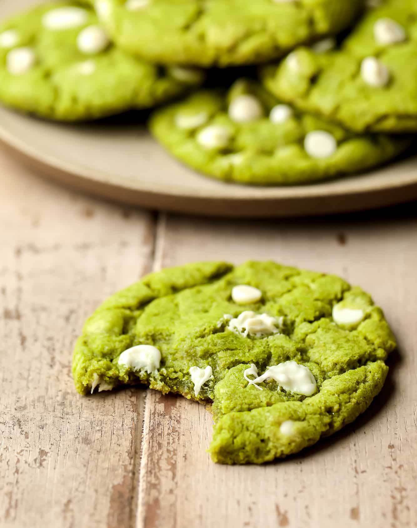 close up on a green white chocolate chip matcha cookie with a bite taken out of it.