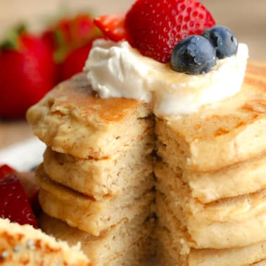 close up on a stack of vegan oat flour pancakes with butter and berries on top.