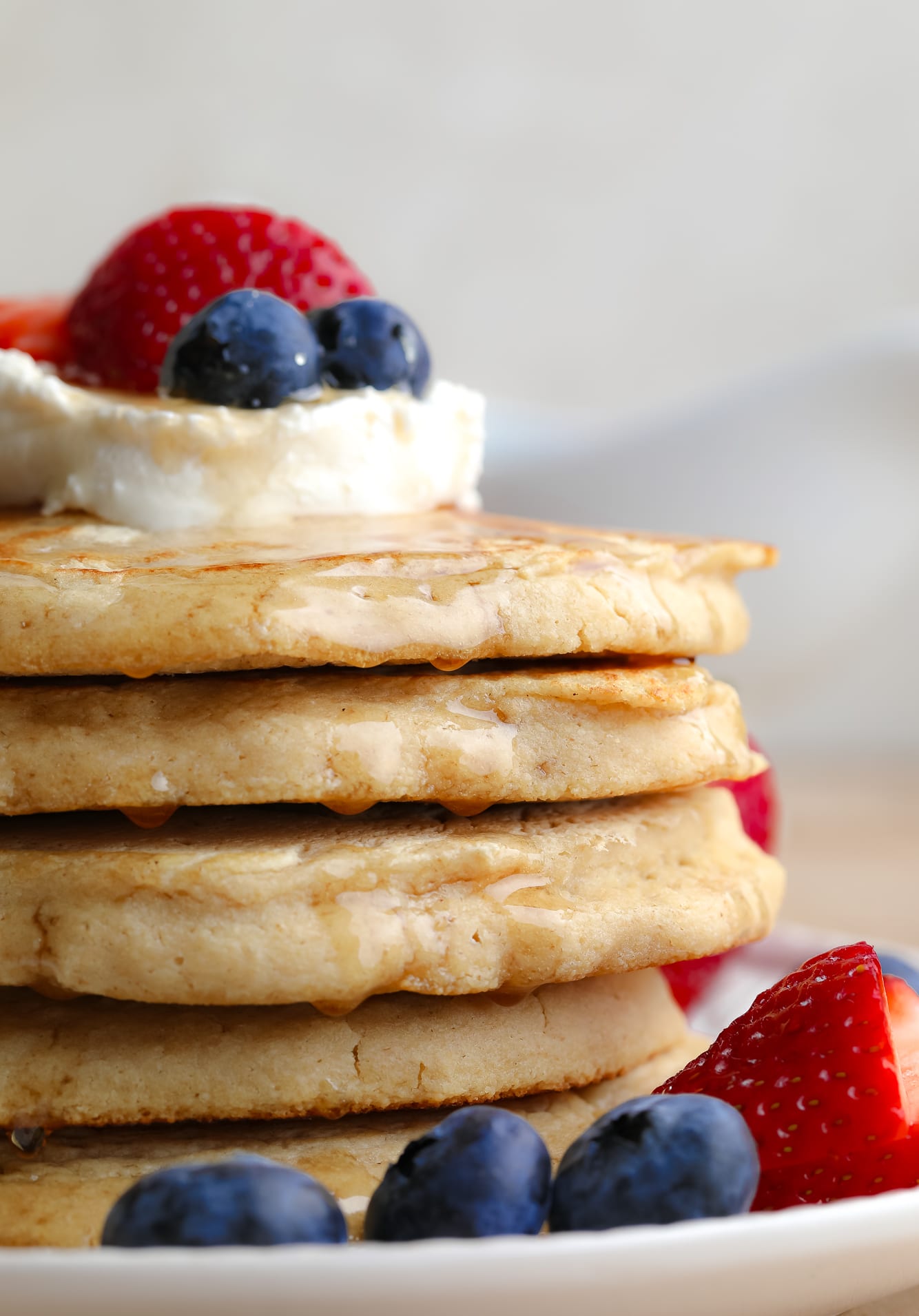 close up on a stack of vegan oat flour pancakes with butter and berries on top.