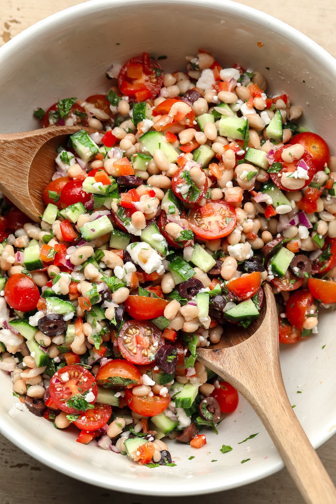 using two wooden spoons to toss a white bean salad together.