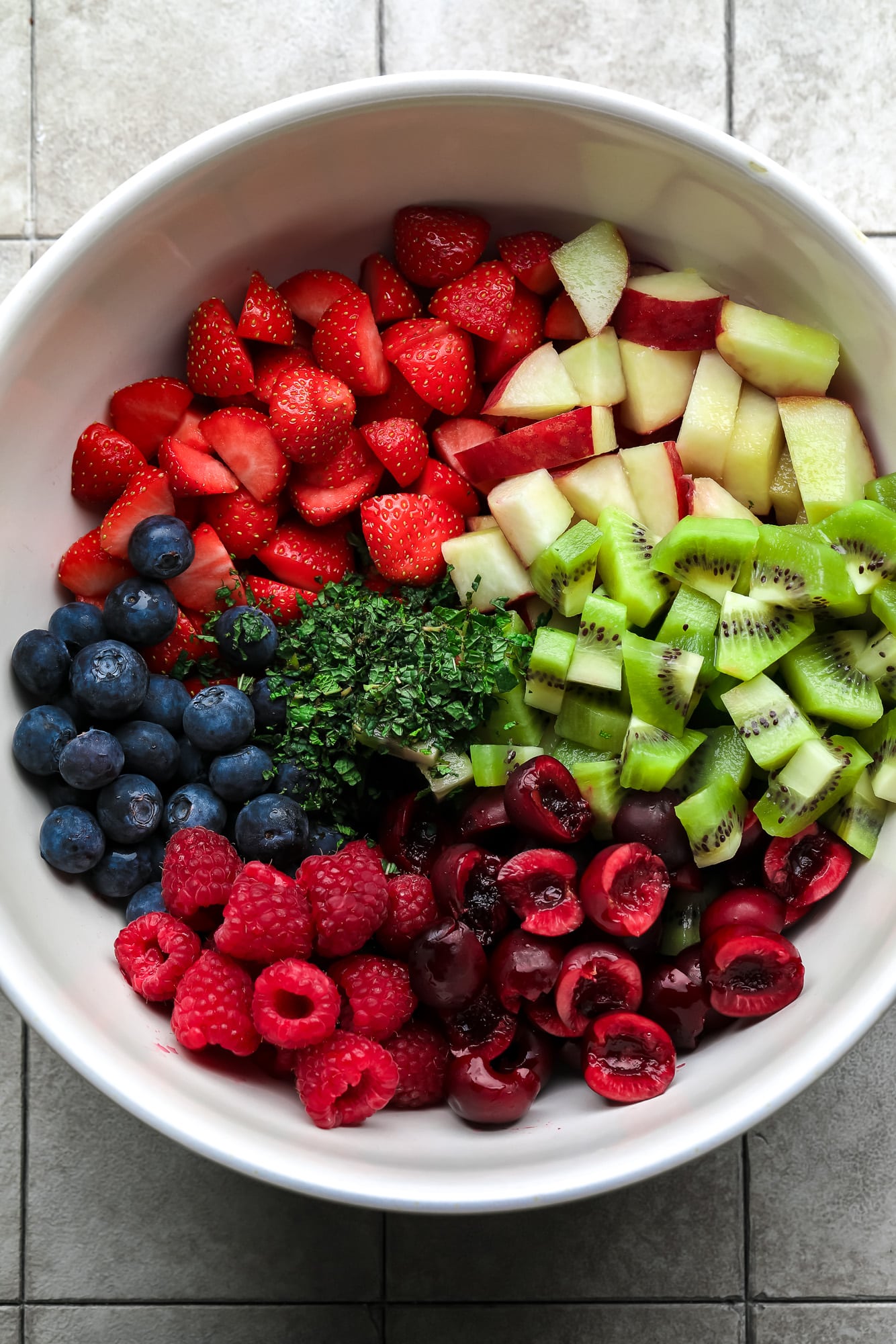 the ingredients for a fruit salad in a large white bowl.