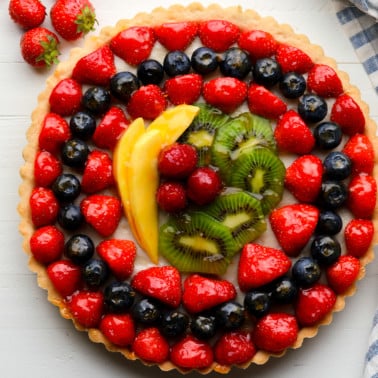 close up on a vegan fruit tart topped with rows of fresh berries, kiwi, and mango.