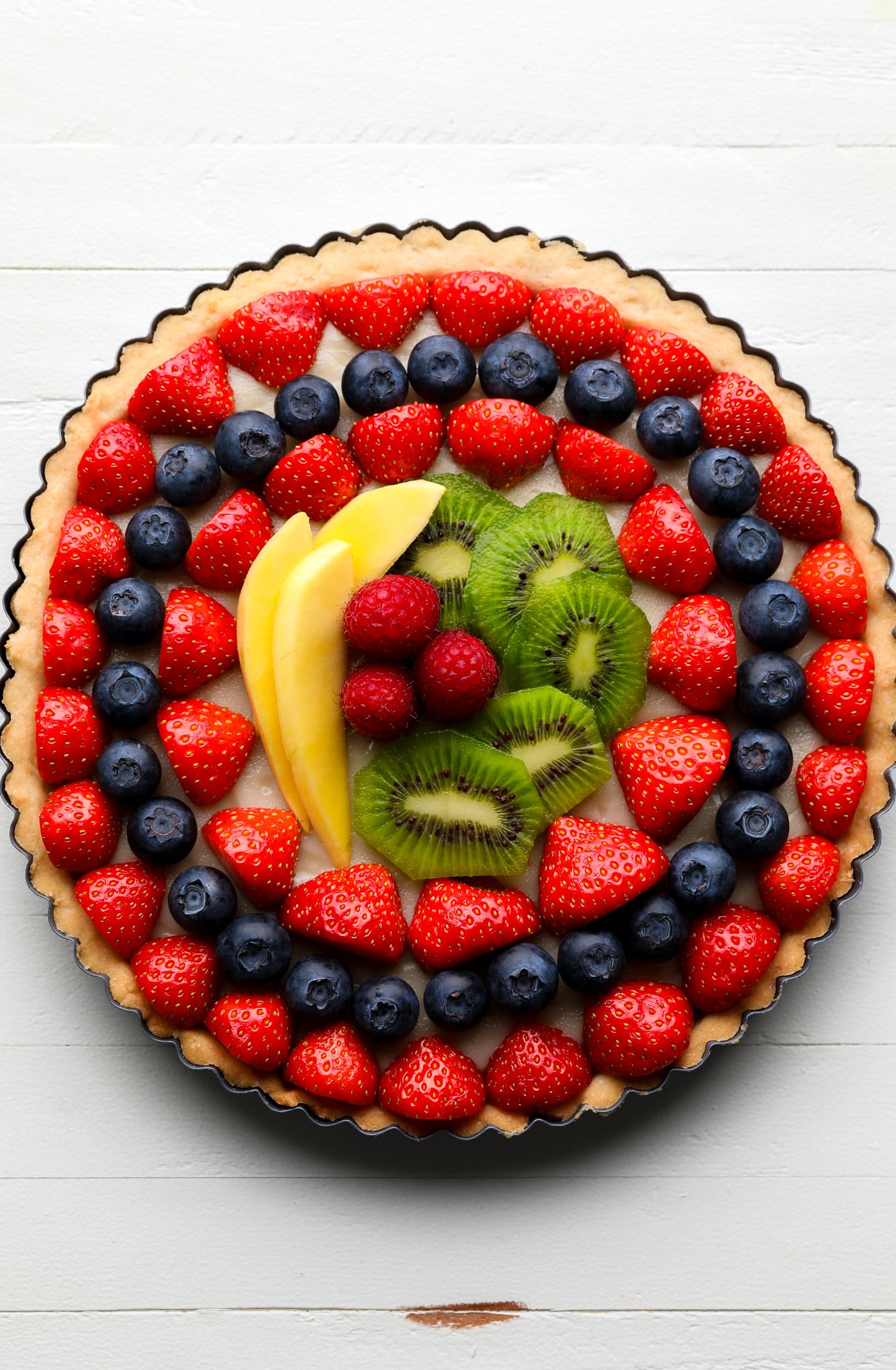 a vegan fruit tart topped with rows of fresh berries, kiwi, and mango.