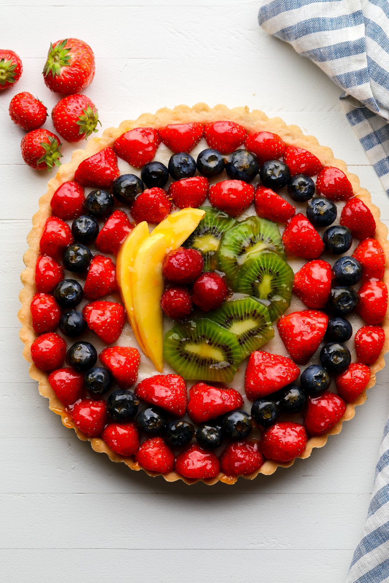 a vegan fruit tart topped with rows of glazed berries, kiwi, and mango.