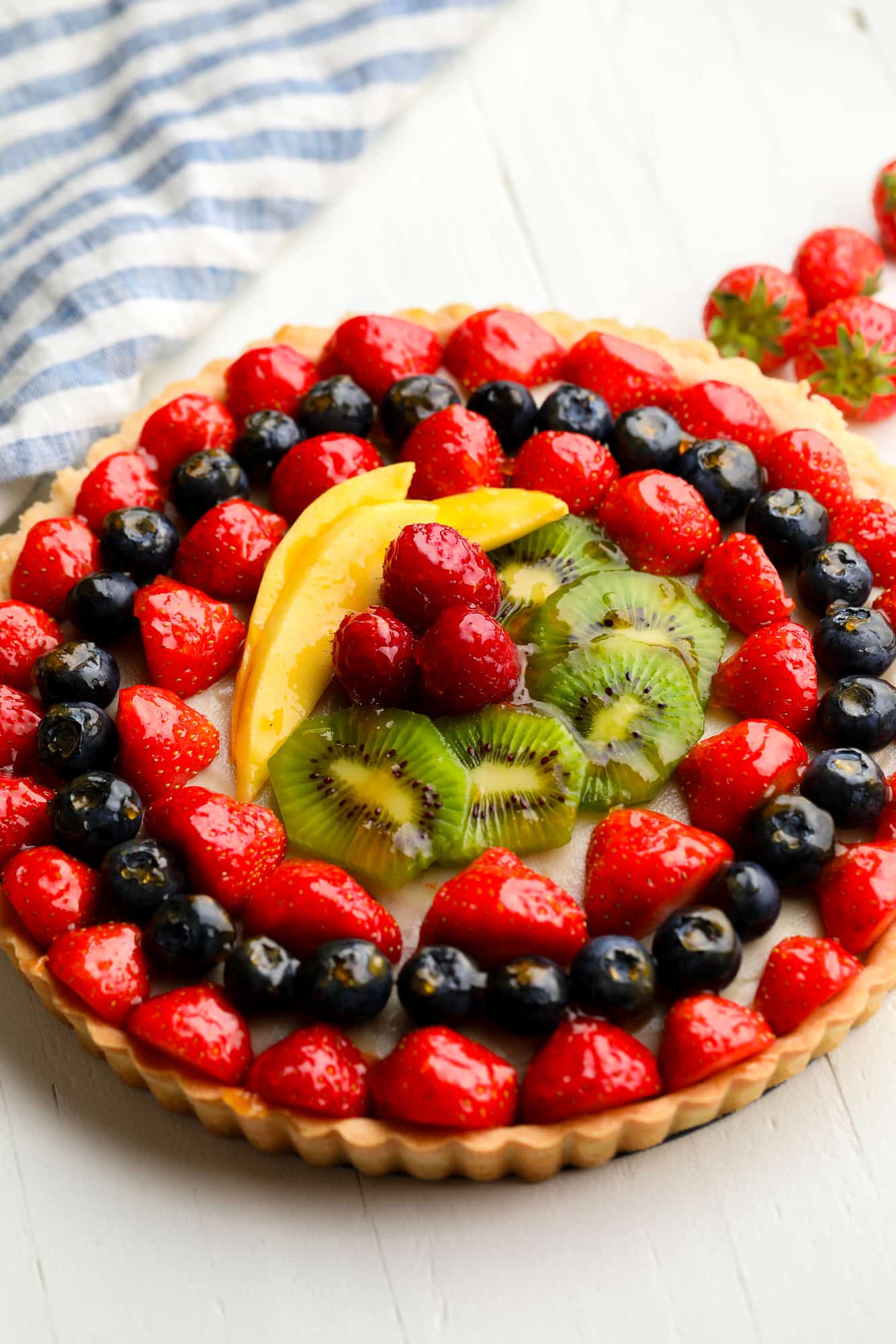 a vegan fruit tart topped with rows of glazed berries, kiwi, and mango.