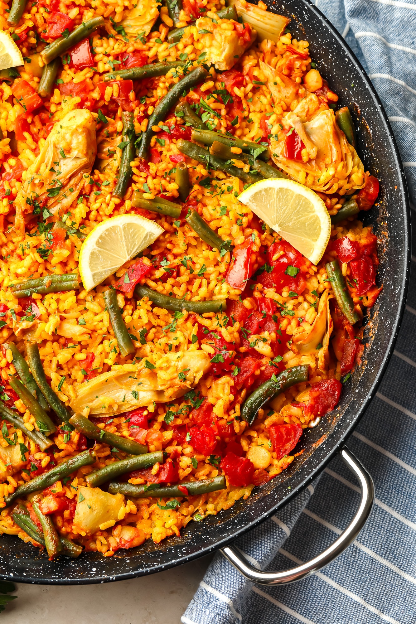 vegan paella topped with lemon slices in a large black paella pan.