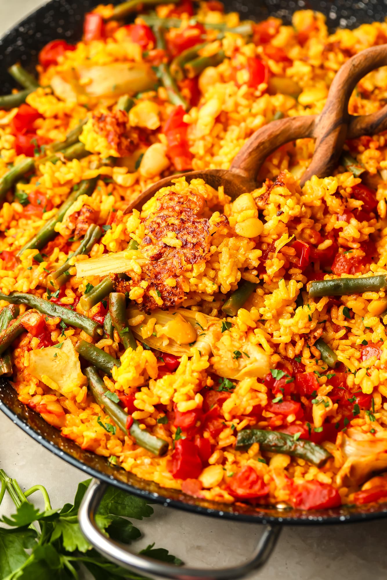 a wooden spoon lifting a scoop of vegan paella out of a large black paella pan.