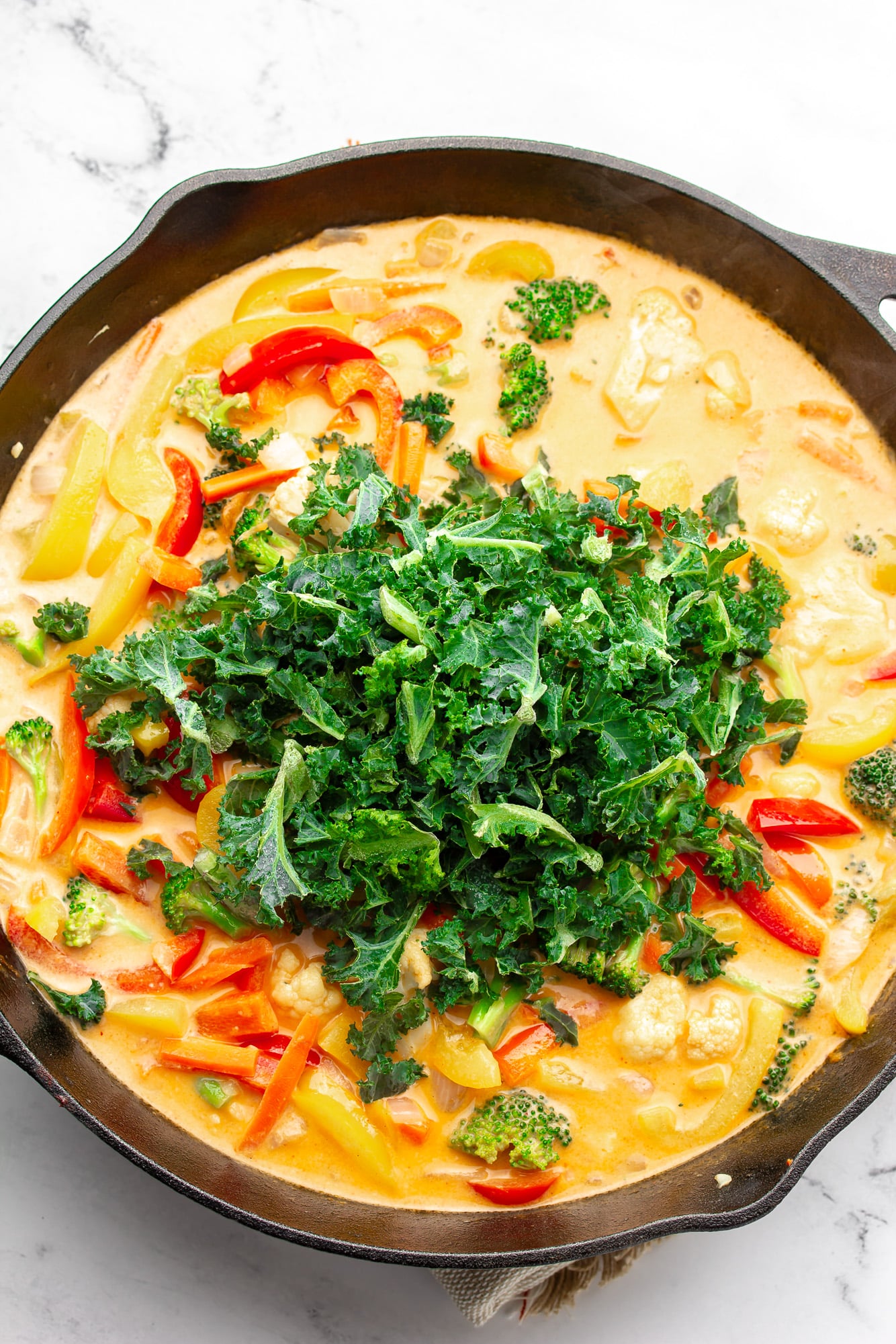 chopped kale on top of red Thai curry in a black skillet.