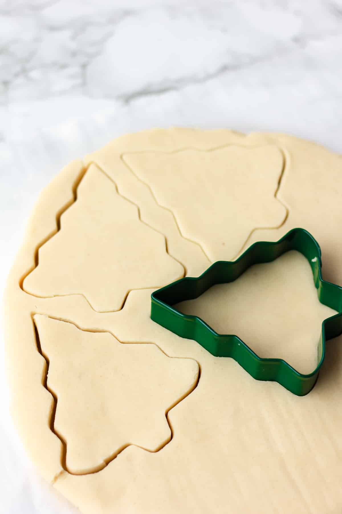 cutting tree shapes out of sugar cookie dough on marble backdrop