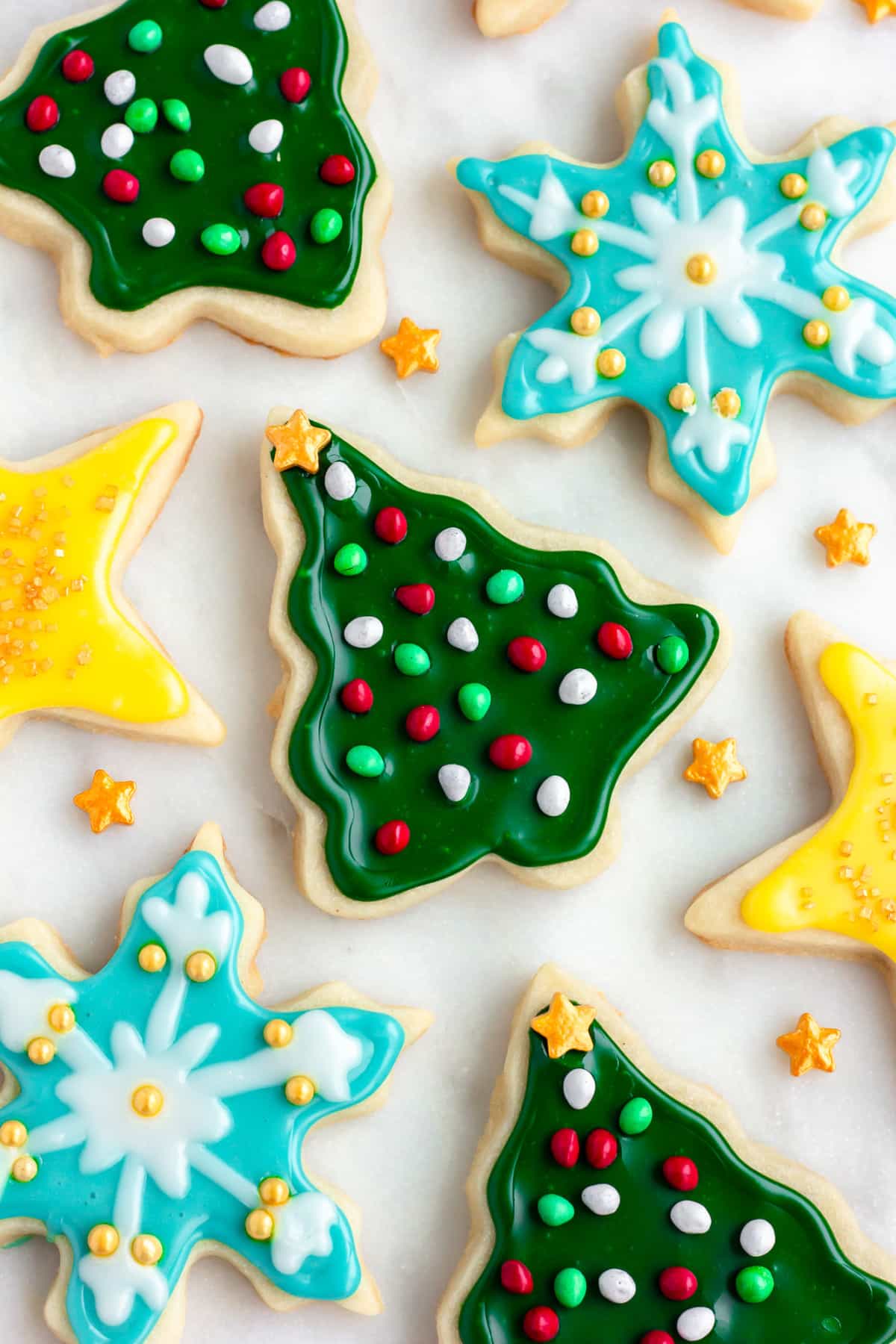 lots of vegan sugar cookies on a white marble background decorated with various colors and sprinkles and shapes