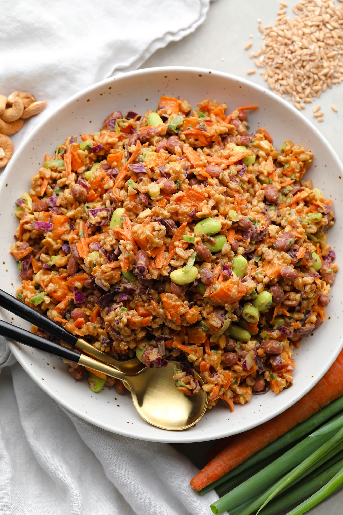 farro salad dressed in peanut sauce in a large white bowl with a gold spoon on the side.