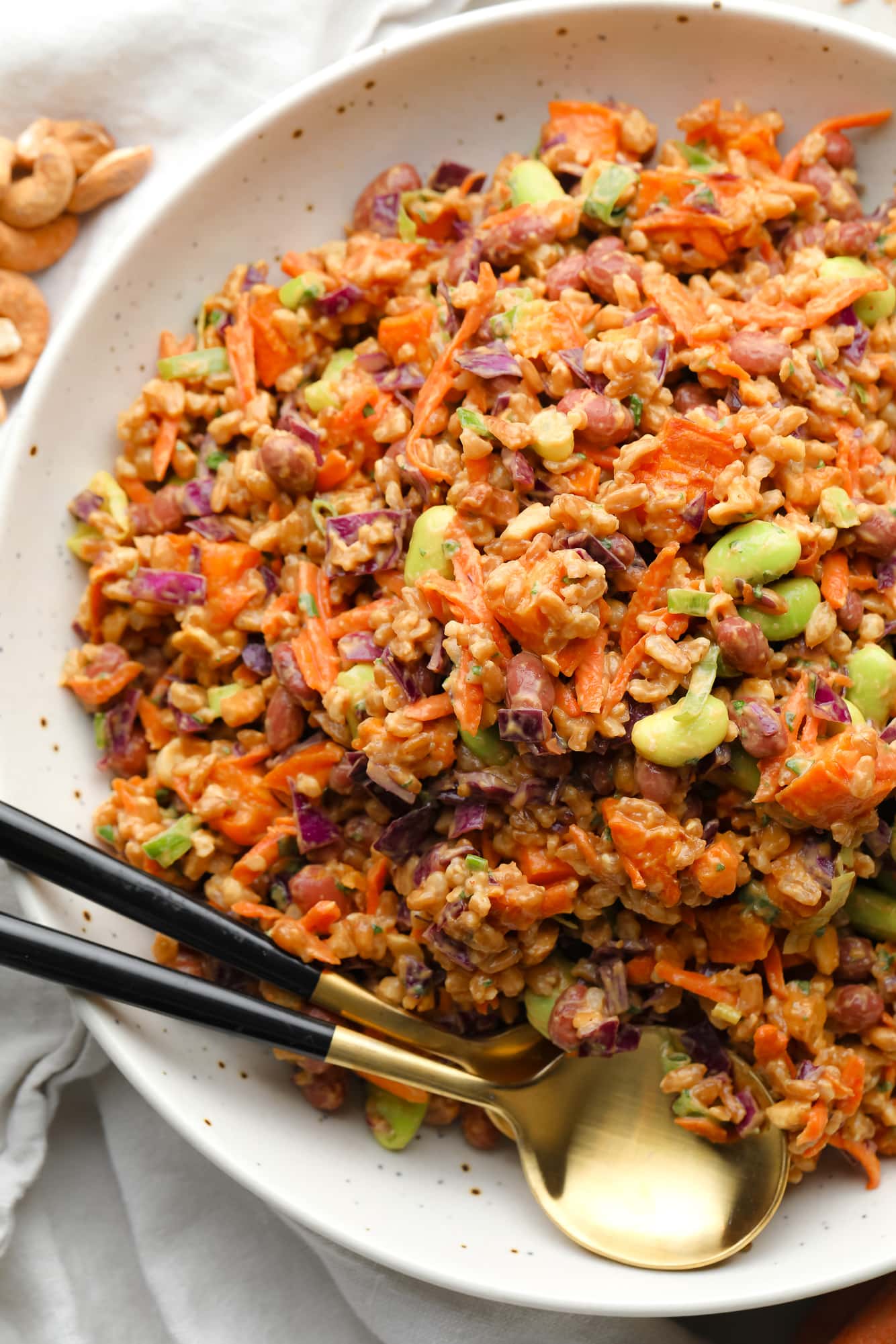 farro salad dressed in peanut sauce in a large white bowl with a gold spoon on the side.