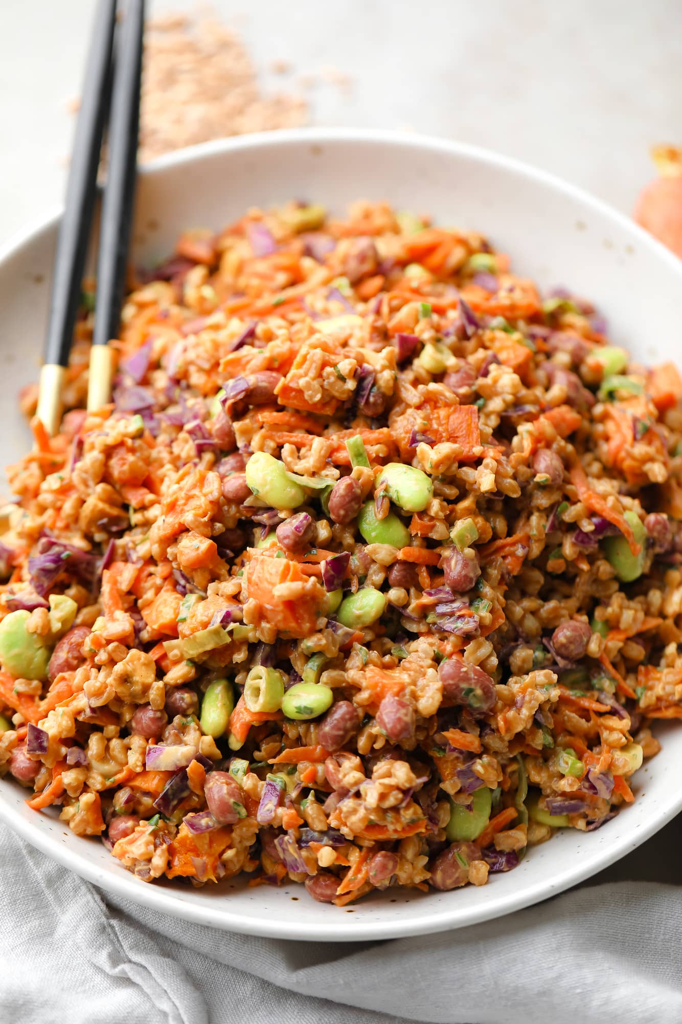 farro salad dressed in peanut sauce in a large white bowl with a gold spoon on the side.