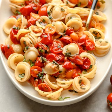 close up on roasted tomato pasta in a white serving dish.