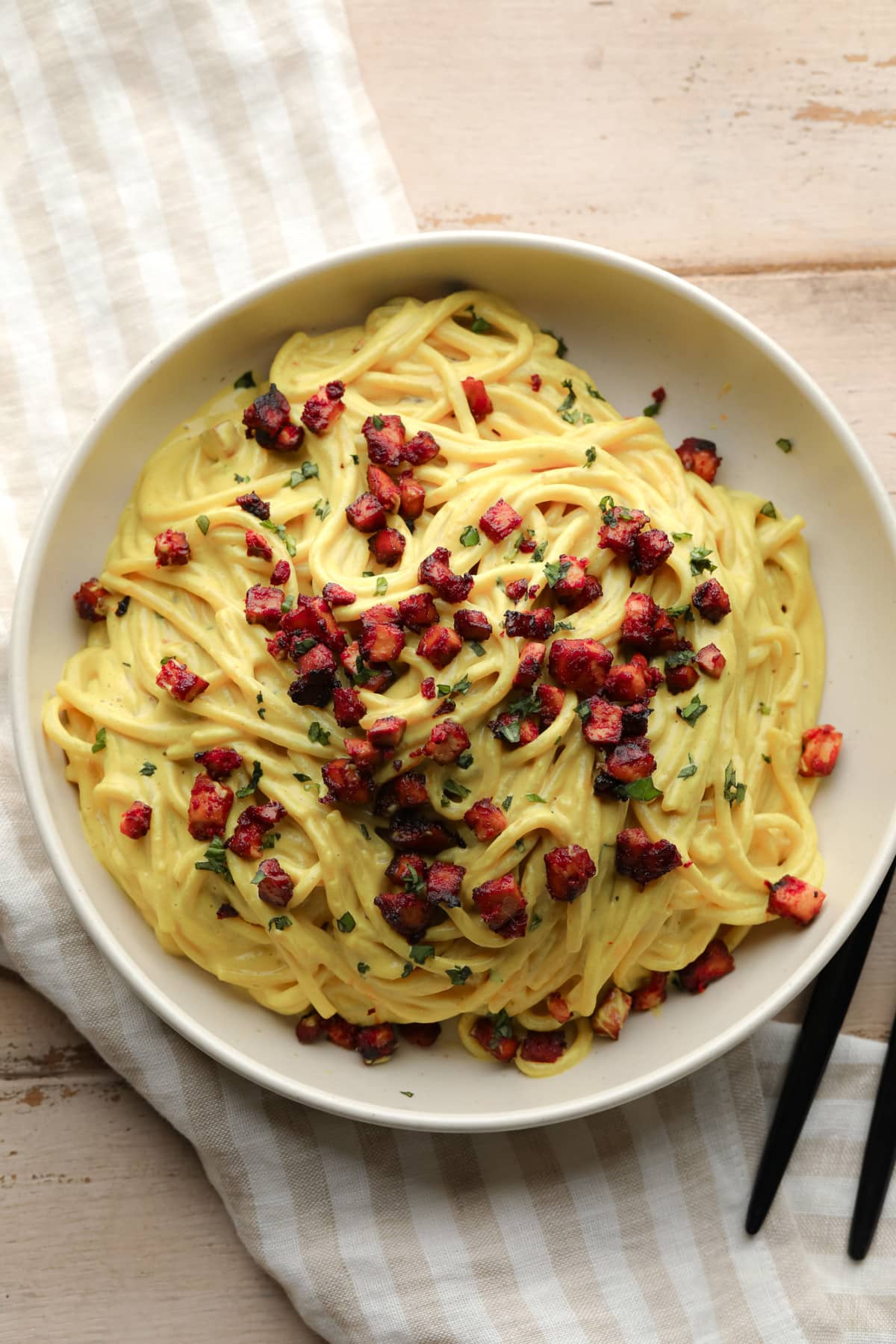 looking down on a bowl of vegan carbonara with tofu bits on wooden background