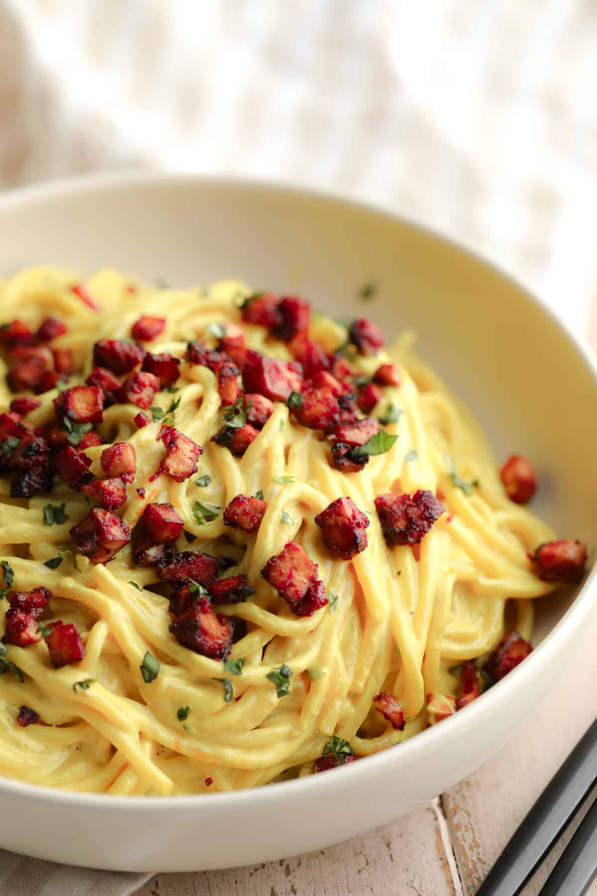 bowl full of yellow noodles with red pieces of tofu on top