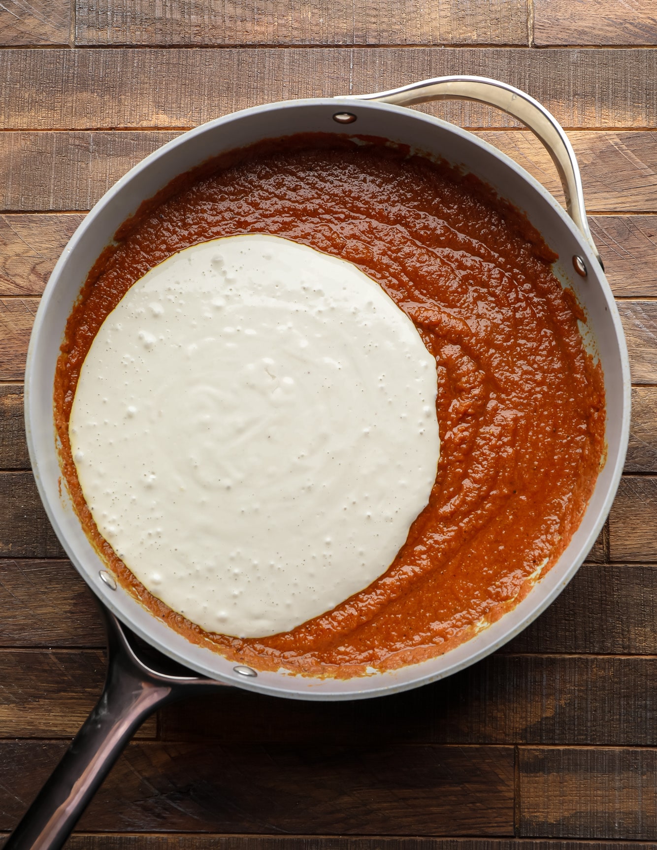 white cashew cream poured into a skillet with tomato puree.