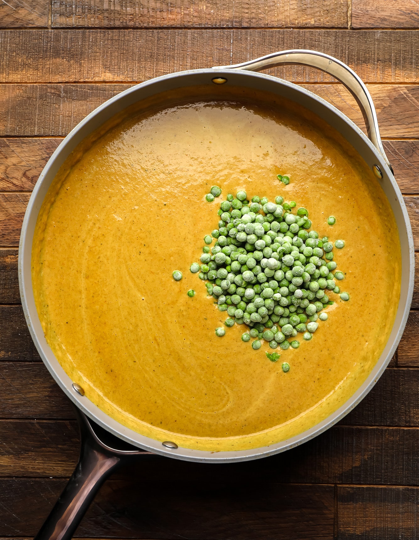 a pile of frozen peas in a yellow sauce in a large skillet.