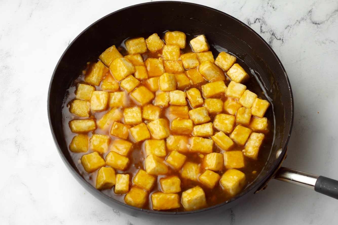 baked tofu cubes in a black skillet with orange sauce.