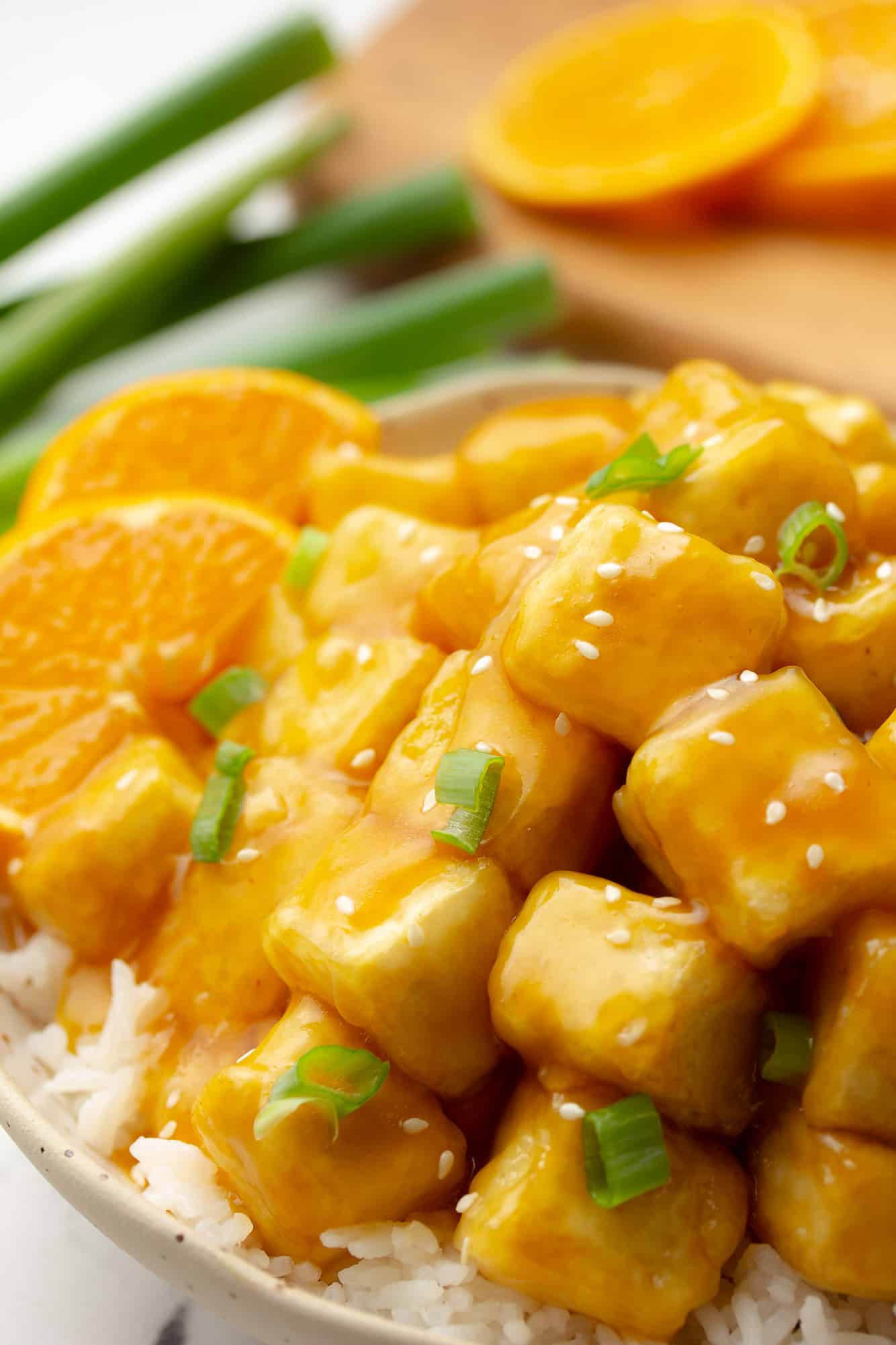 close up on orange tofu with orange slices on the side and sliced green onions on top.