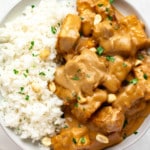 close up on peanut tofu and coconut rice topped with peanuts and cilantro in a white bowl.