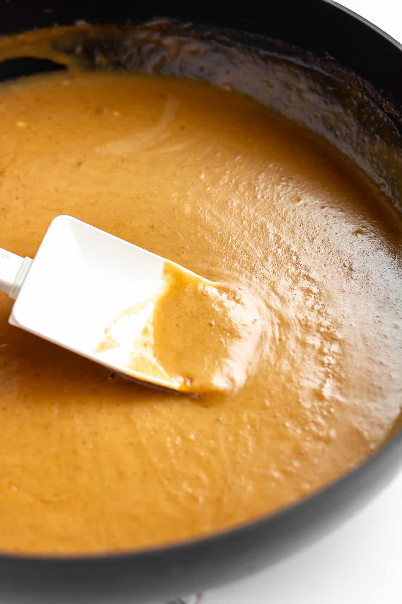 a white spatula stirring peanut sauce in a black skillet.