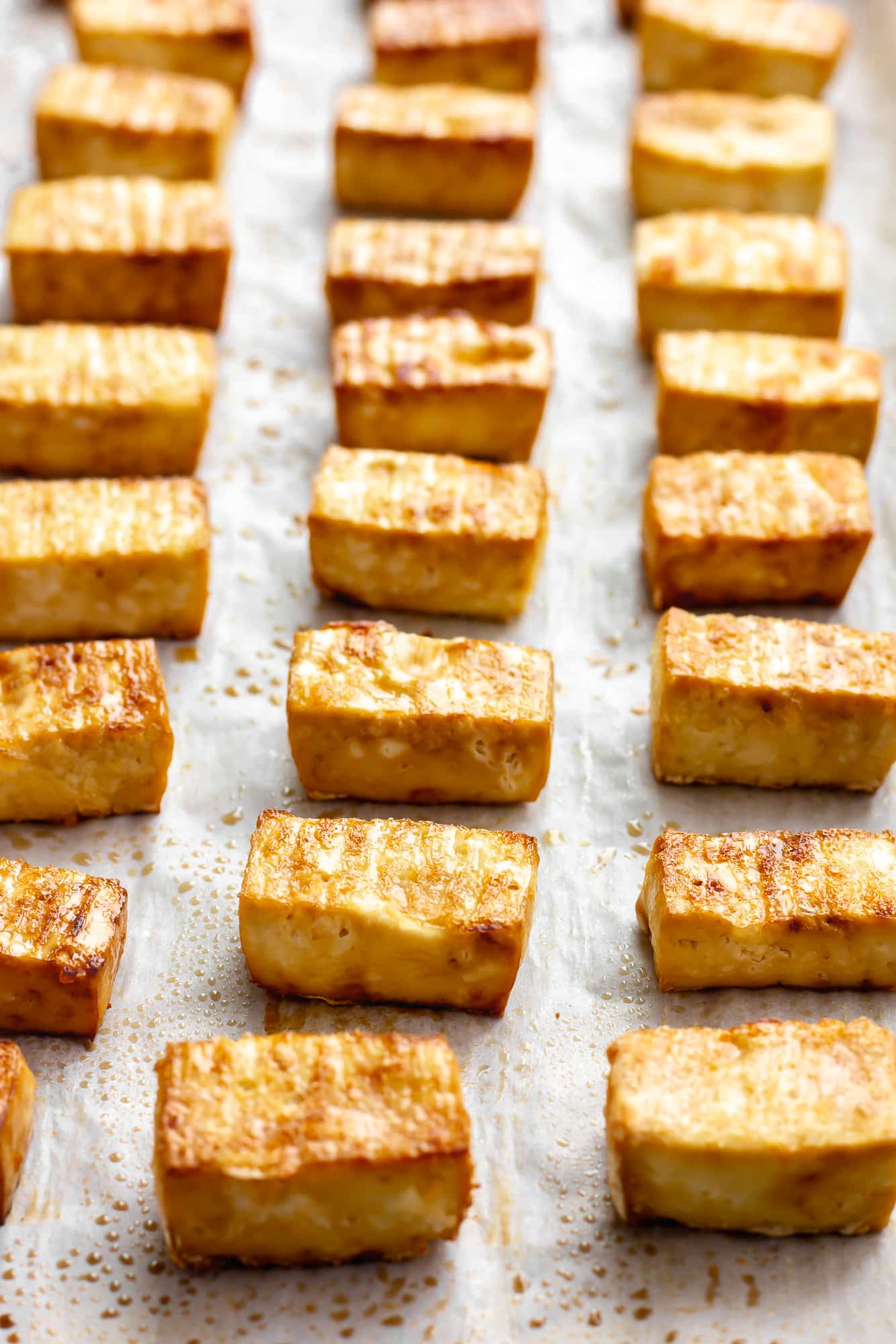 baked tofu cubes in rows on a parchment-lined baking sheet.