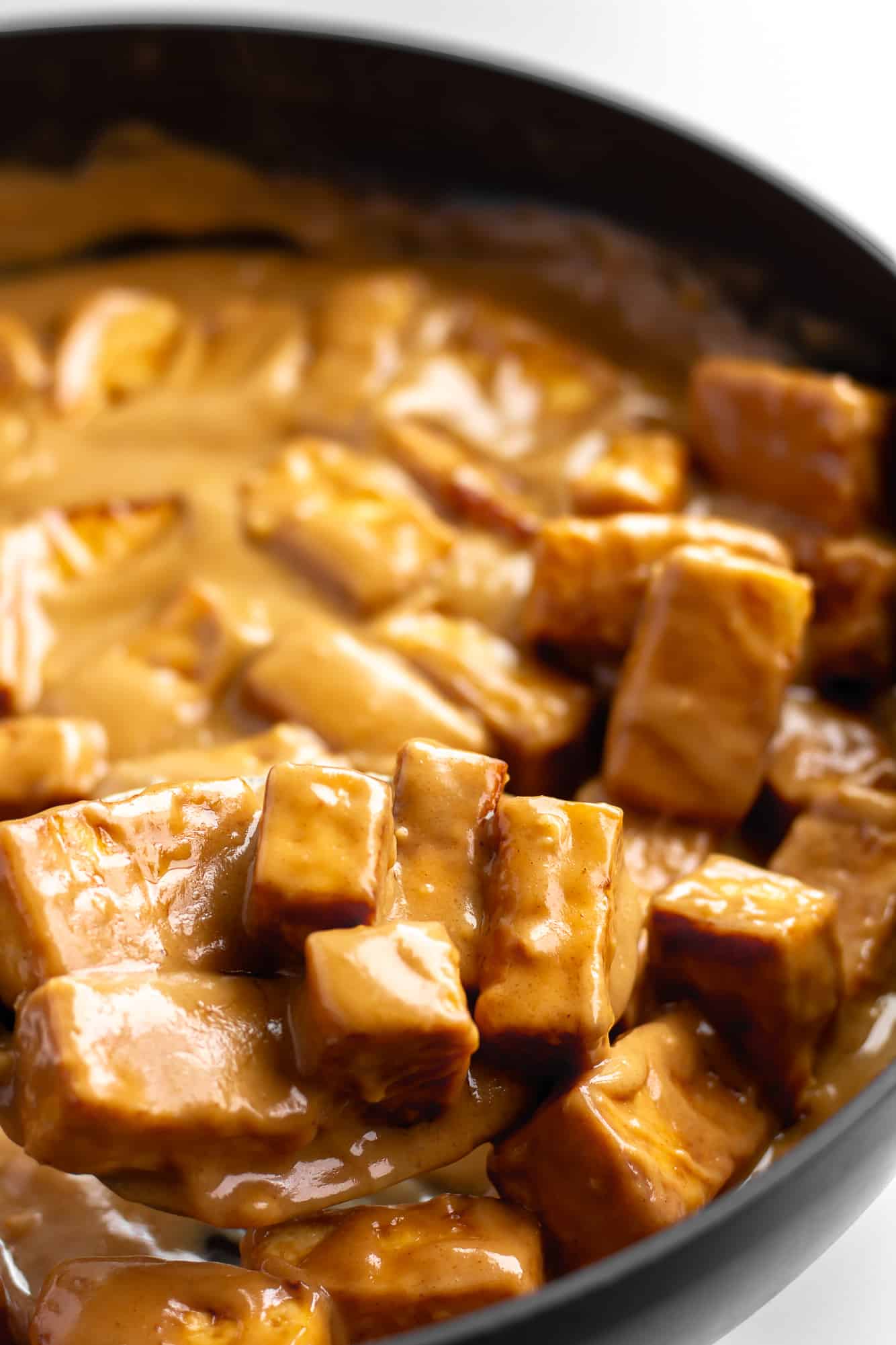 bake tofu cubes tossed in peanut sauce in a black skillet.