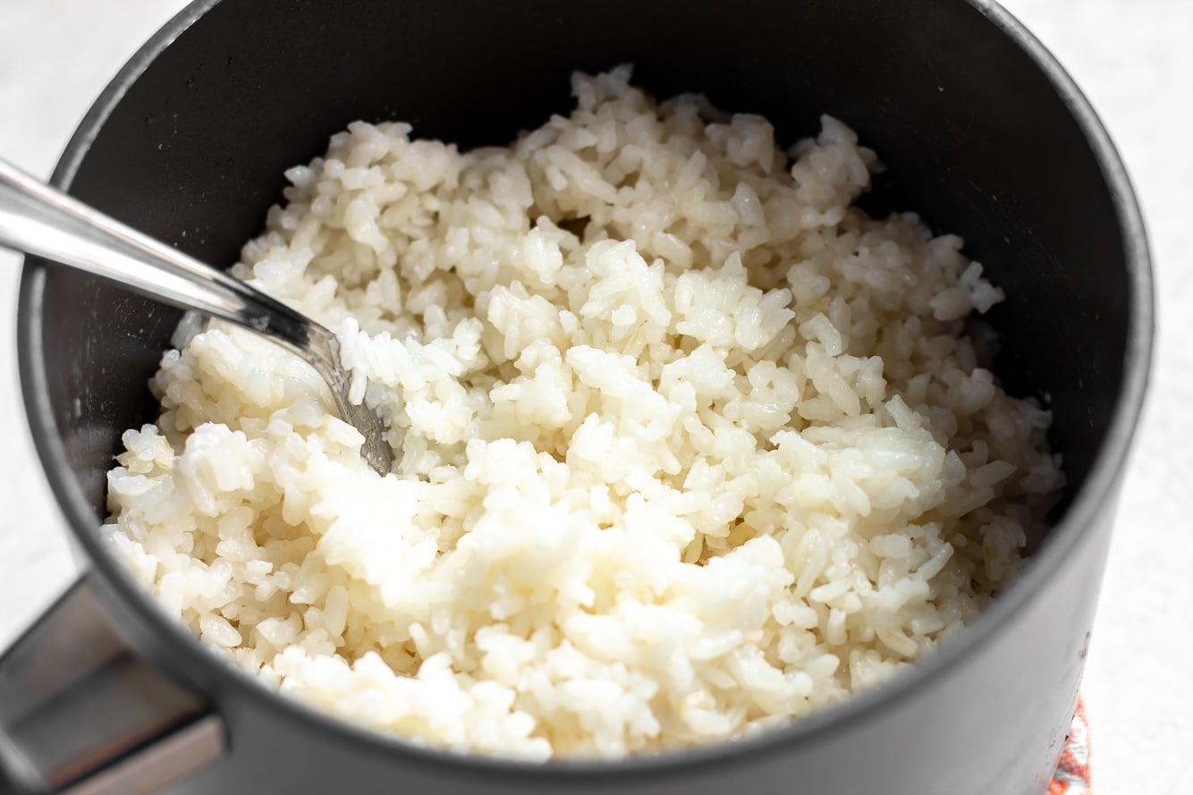 fluffing coconut rice with a fork in a black pot.