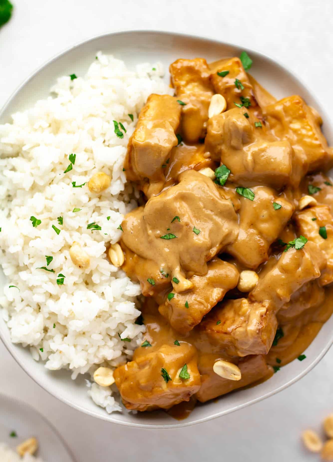 peanut tofu and coconut rice topped with peanuts and cilantro in a white bowl.