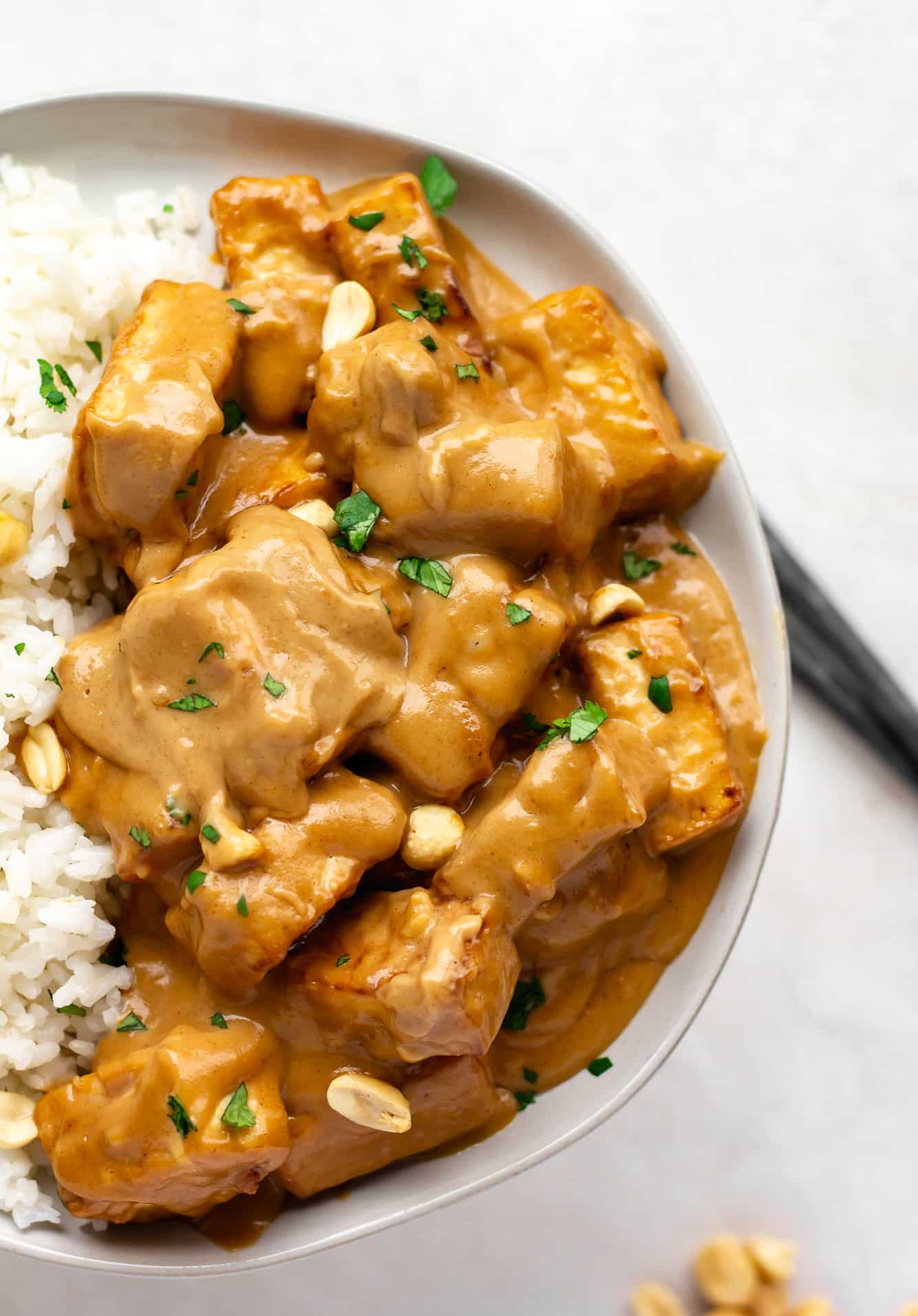 peanut tofu and coconut rice topped with peanuts and cilantro in a white bowl.