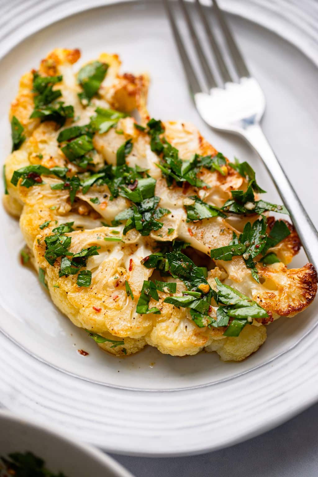 plate and fork with a cauliflower steak on it with green herbs