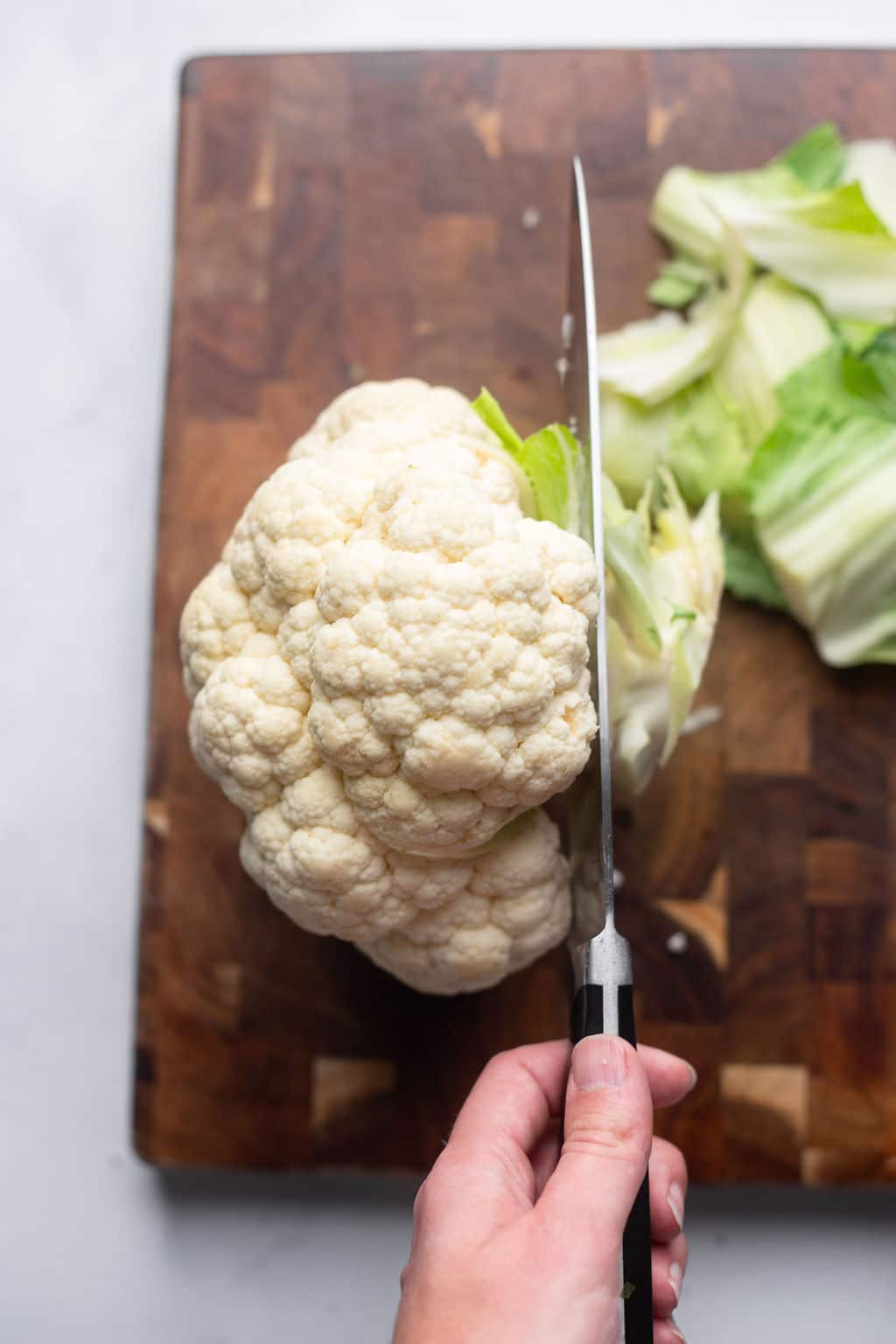 a knife cutting off the stem of a whole cauliflower