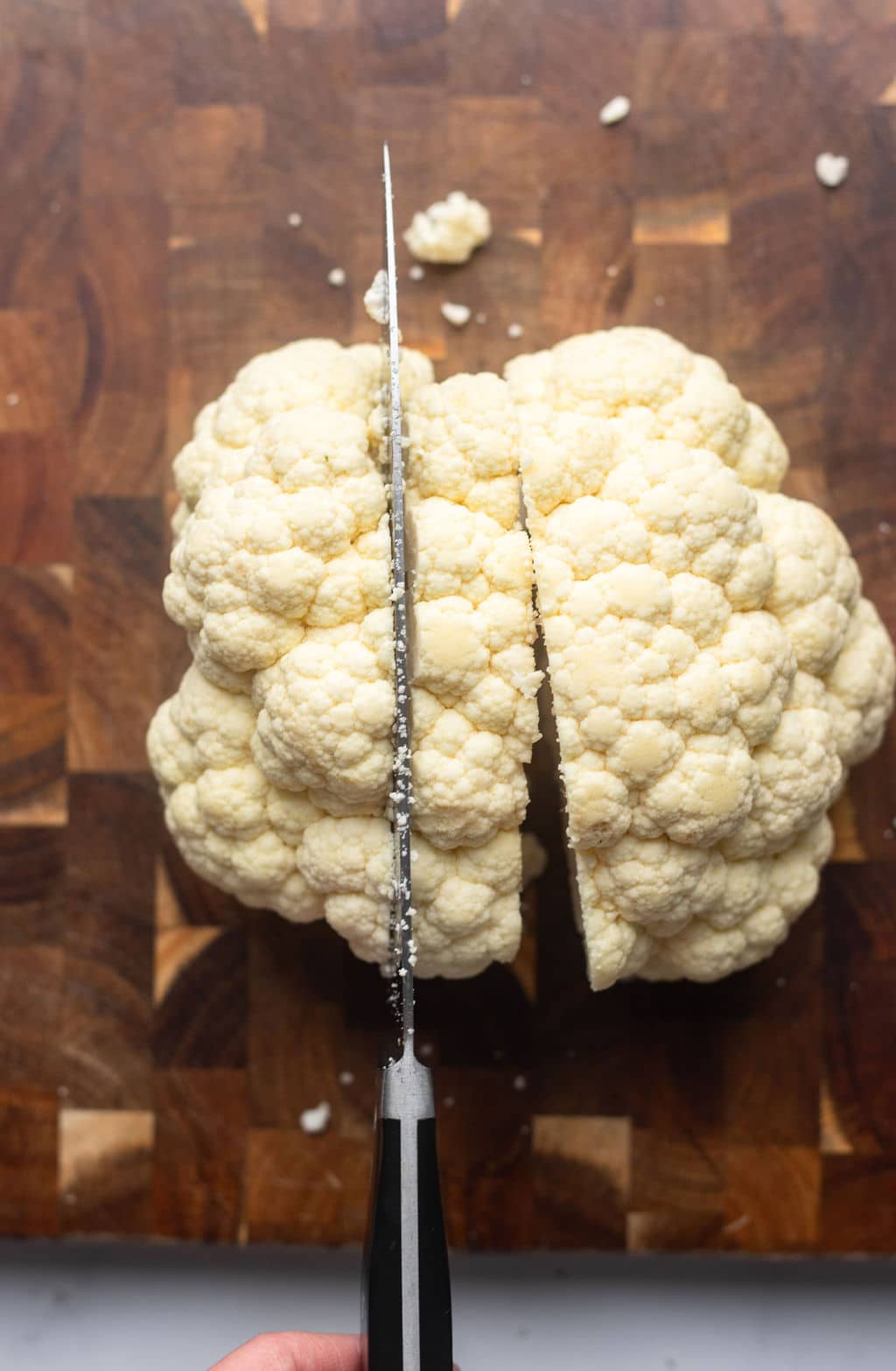 showing a knife cutting slices of cauliflower from whole