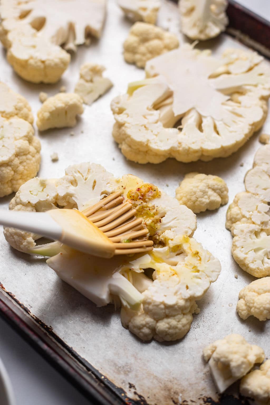 brushing on olive oil garlic mixture onto cauliflower pieces