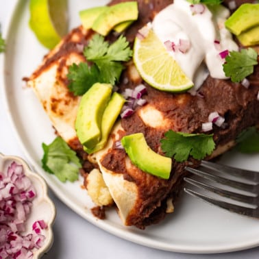 close up on Roasted Veggie Enchiladas with Black Bean Sauce on a white plate with a fork on the side.