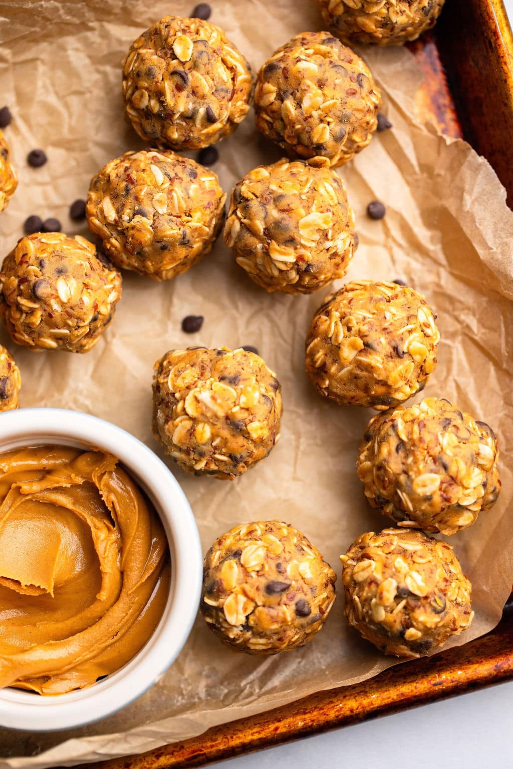 close up on peanut butter energy balls next to a small bowl of peanut butter on a parchment lined baking sheet.