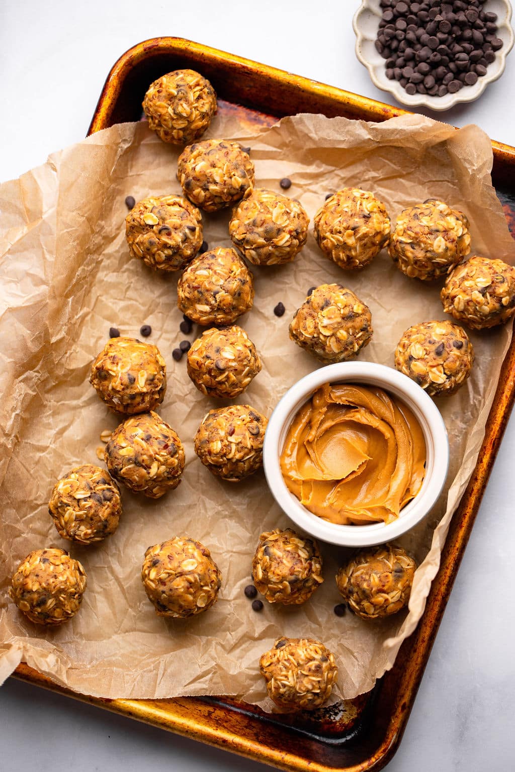 peanut butter energy balls next to a small bowl of peanut butter on a parchment lined baking sheet.