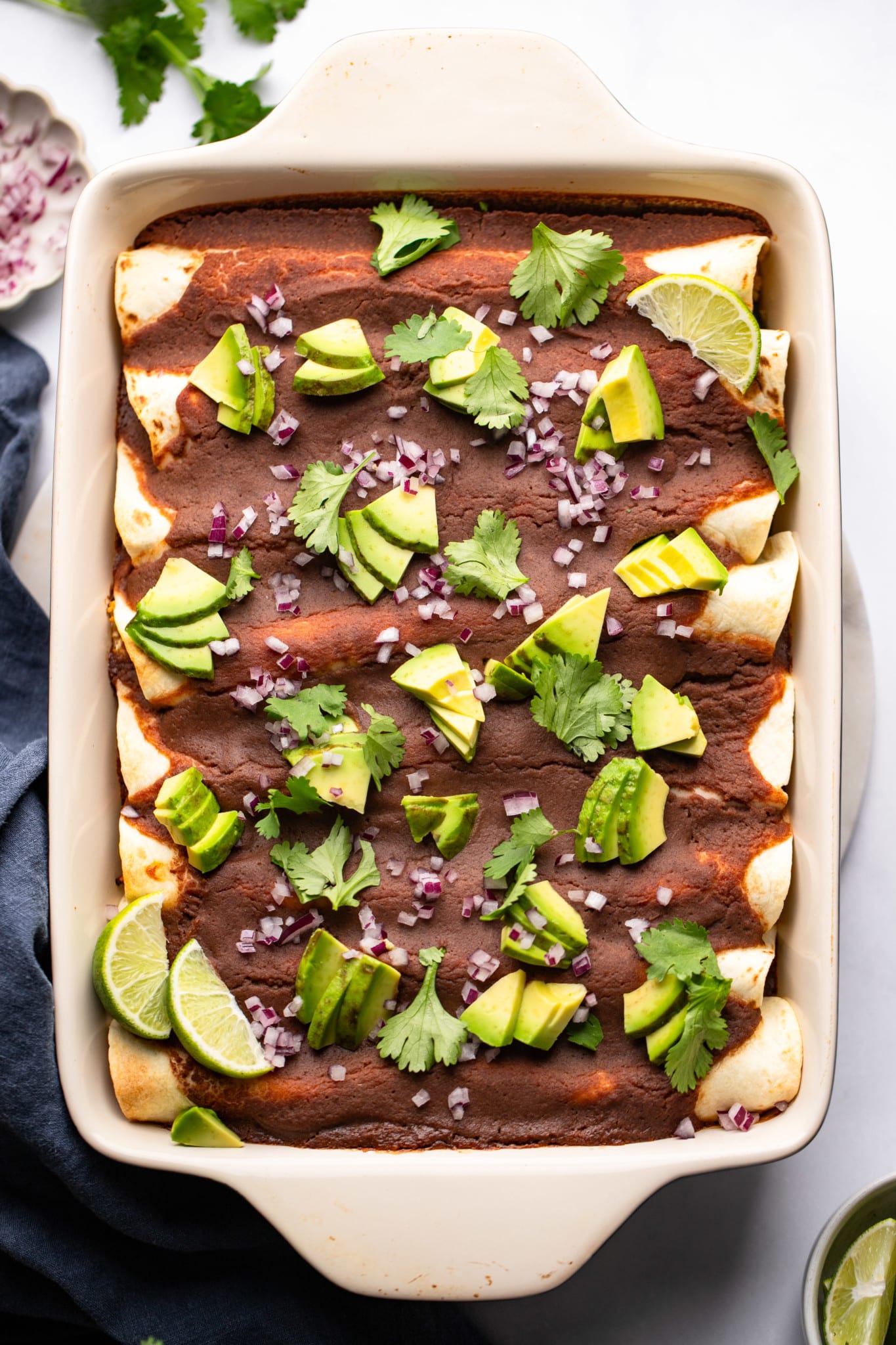 Roasted Veggie Enchiladas with Black Bean Sauce topped with avocado, onions, and cilantro in a baking dish.